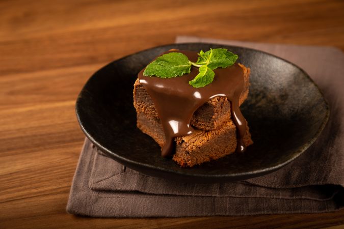 Two chocolate brownies with chocolate syrup and fresh mint leaves served on plate