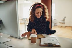 Woman with curly hair smiling with notes and a coffee at work
