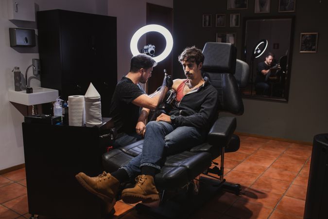 Master doing tattoo on forearm of male customer