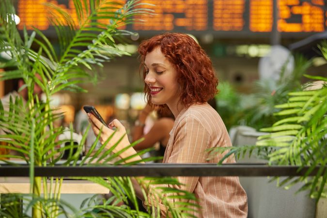 Cheerful young woman working on laptop in cafe and browsing phone