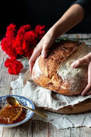 Crop person putting sourdough bread near flowers and honey