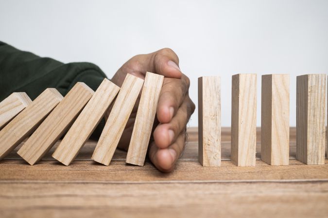 male hand stop falling wooden blocks. domino effect or risk protection strategy concept