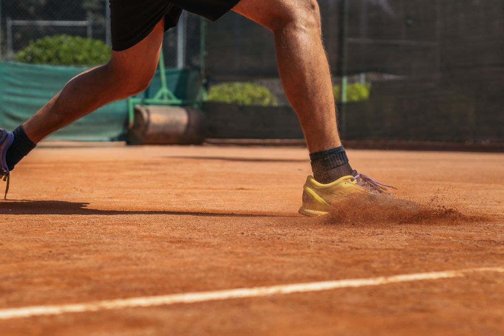 Man in sportswear playing tennis on a dirt tennis court