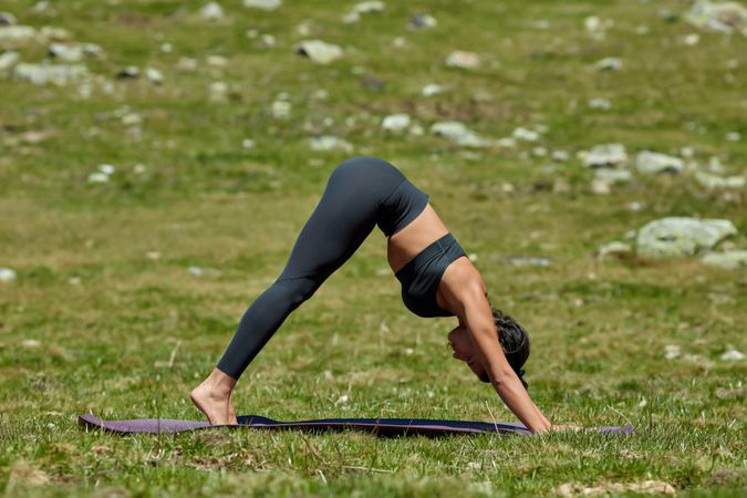 Woman in gray yoga outfit doing downward dog pose with bare feet in a mountain valley