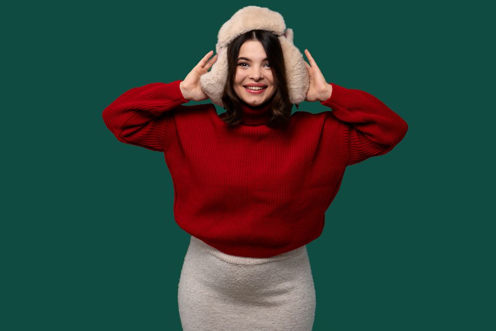 Cheerful woman in red sweater holding fur hat with hands