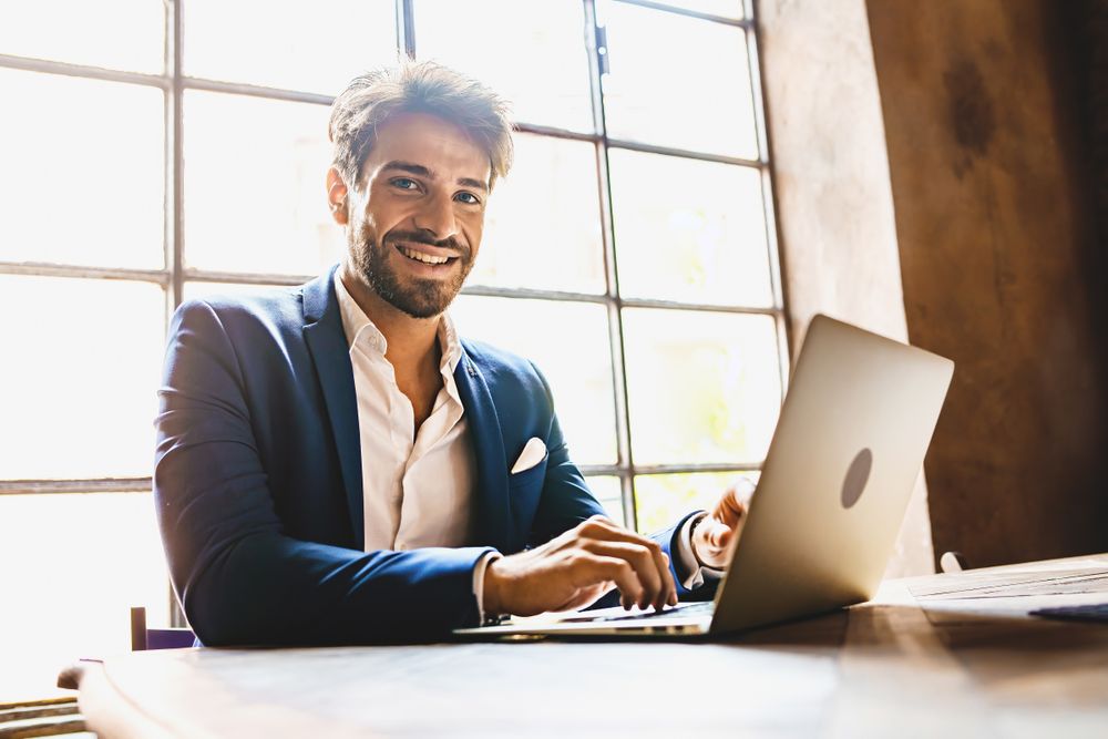 Happy businessman typing on a laptop computer in front of a window
