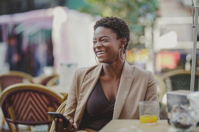 Smiling Black woman with smartphone sitting at table in cafe