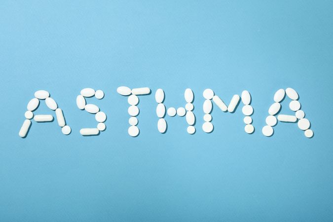 Pills on blue background spelling out “asthma”