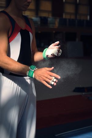 Unrecognizable sportsman preparing himself by putting magnesium in his hands to do the exercises of sport gymnastics.