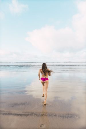 Woman in swimwear running near sea