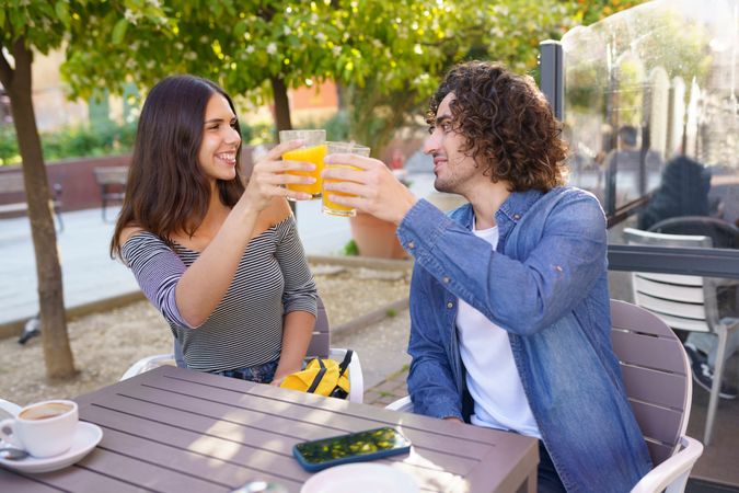 Man and woman toasting with their orange juice while looking at each other outside