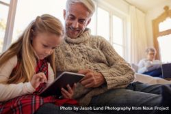 Senior man with granddaughter using digital tablet at home 0v3wWg