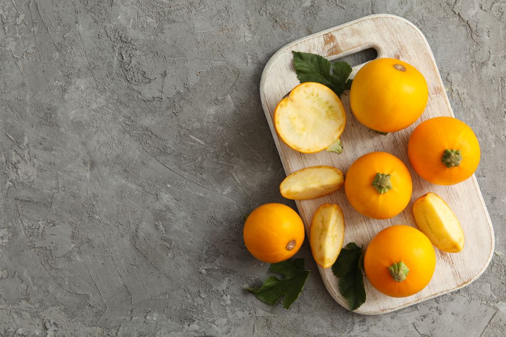Board with round zucchini and leaves on gray background