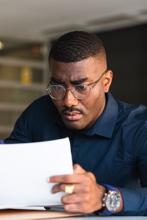 Black man writing in notepad near laptop in office