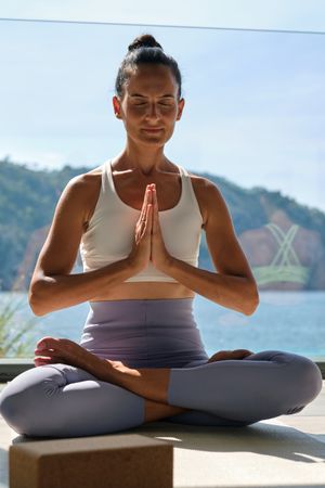Female sitting in lotus position with closed eyes on terrace in sunlight