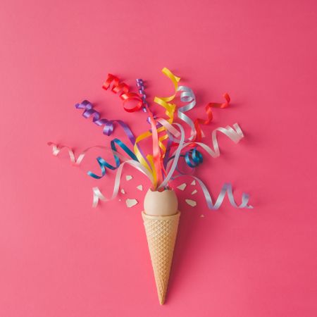 Ice cream cone with egg and party streamers on pink background