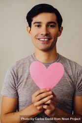 Romantic happy Hispanic male holding cut out pink heart to his chest, vertical 4MaJE4
