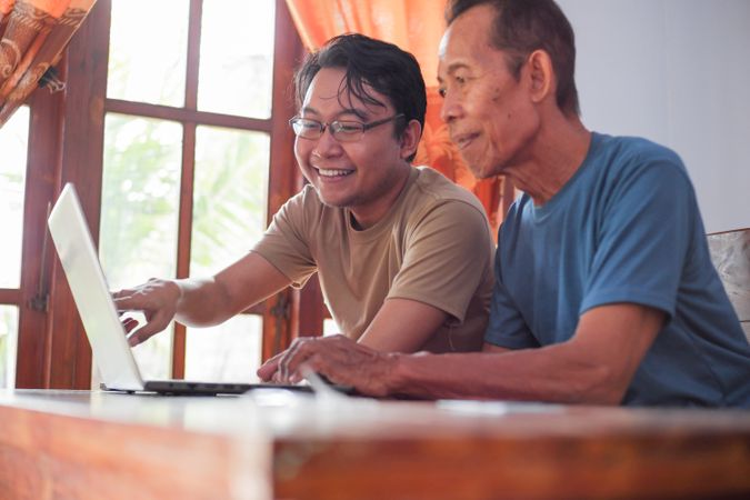 Happy adult son teaching mature father using laptop