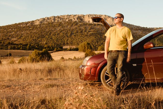 Man leaning in broken car in countryside