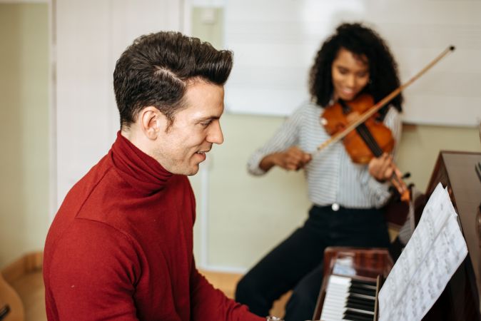 Man playing piano near woman playing violin in studio
