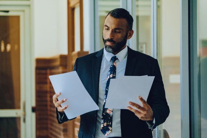 Serious businessman in suit and tie reviewing papers standing in office