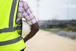 Back view of man in green vest holding a bump cap under his arm