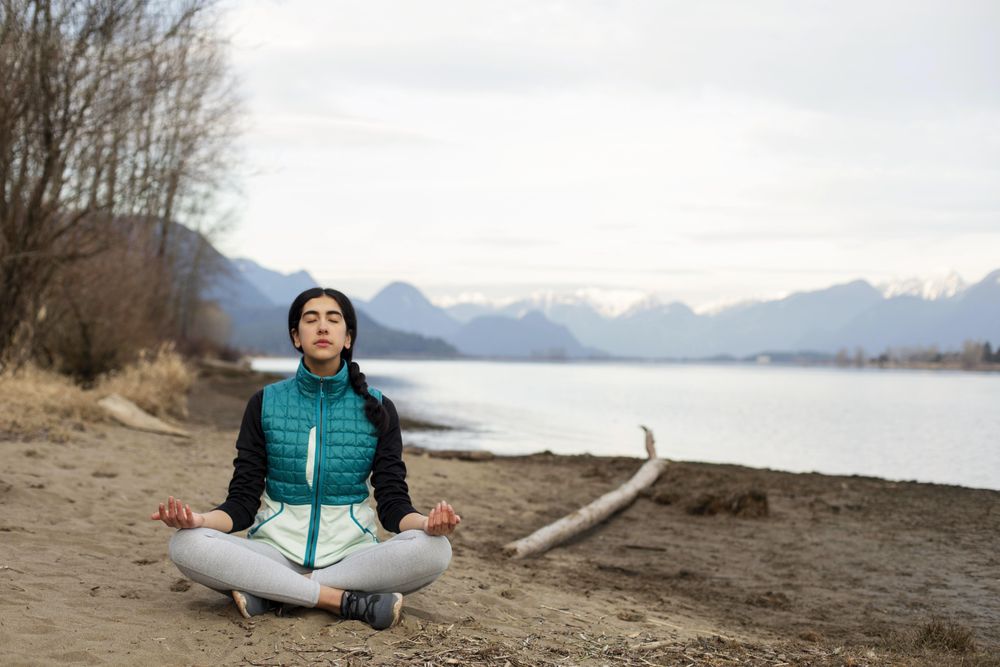 Young woman meditating on the lake shore