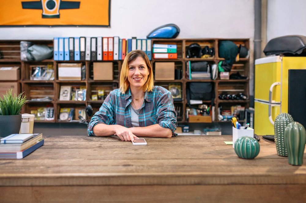 Portrait of smiling blonde young female employee looking at camera behind of industrial shop counter
