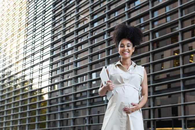 Smiling Black woman with laptop coming out of office building