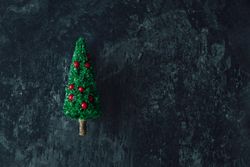 Miniature Christmas tree with red baubles on dark marble table