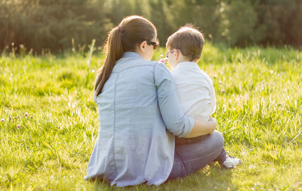 Cute son giving a bouquet of flowers to his mother sitting in a field
