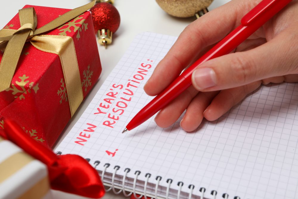 Notepad with text, pen in hand and gift box on light background, close up