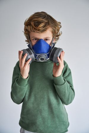Kid in half face respirator and looking at camera in gray studio