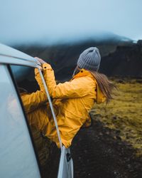 Woman in yellow jacket sitting on car window