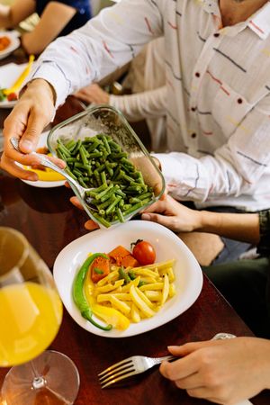 Cropped image of person holding green vegetable dish sitting at dinner table