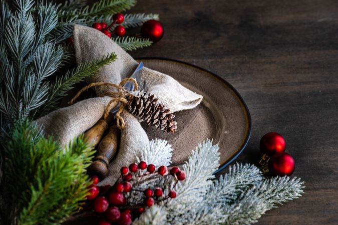 Rustic table setting for Christmas nestled on table with pine and red baubles