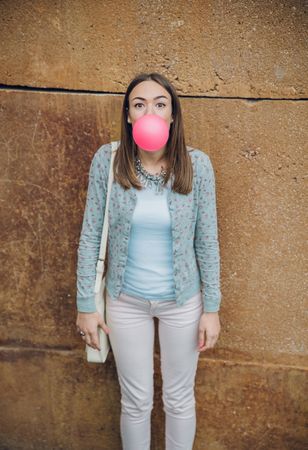 Woman standing in front of stone wall blowing bubble gum