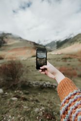 Woman taking photo on smartphone of valley with high hills in cloudy weather