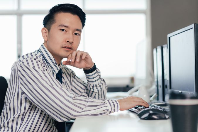 Asian male employee working on computer at desk in the office