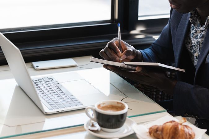 Anonymous focused Black male entrepreneur taking notes during work in cafe