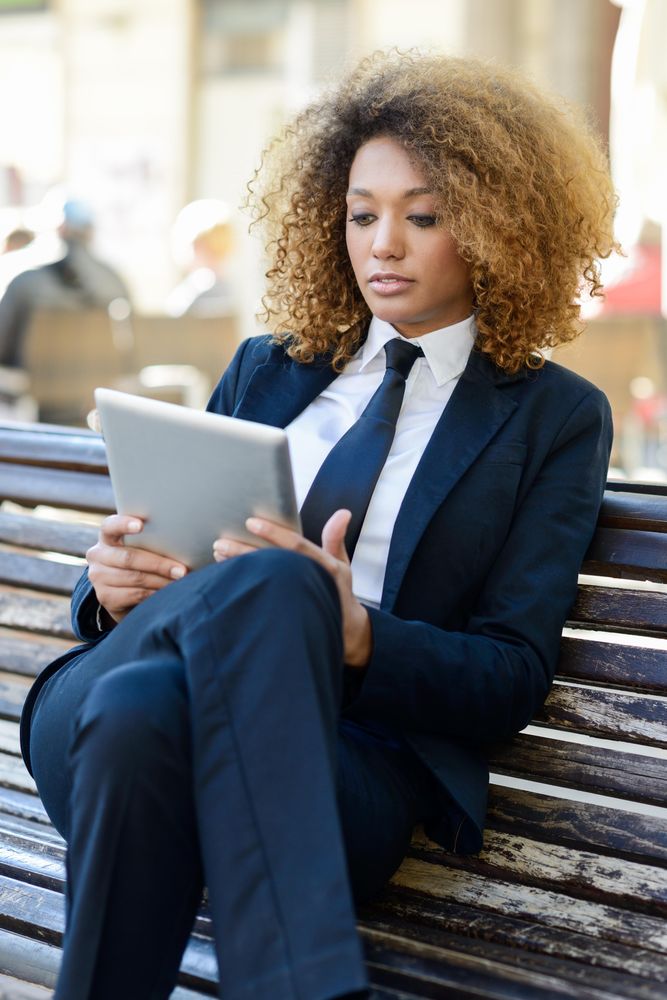 Woman in suit using her digital tablet on outdoor bench