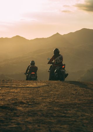 Two people riding mountain motorcycle on brown field at sunset