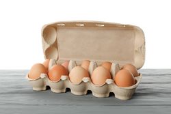 Few raw chicken eggs in carton box on wooden table against light background