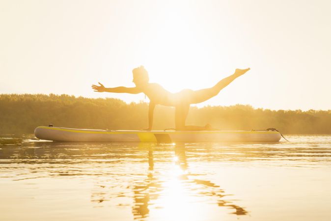 Woman doing yoga balance on paddle board at dawn
