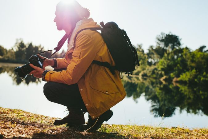 Man shooting photos of nature sitting beside a lake on a sunny day