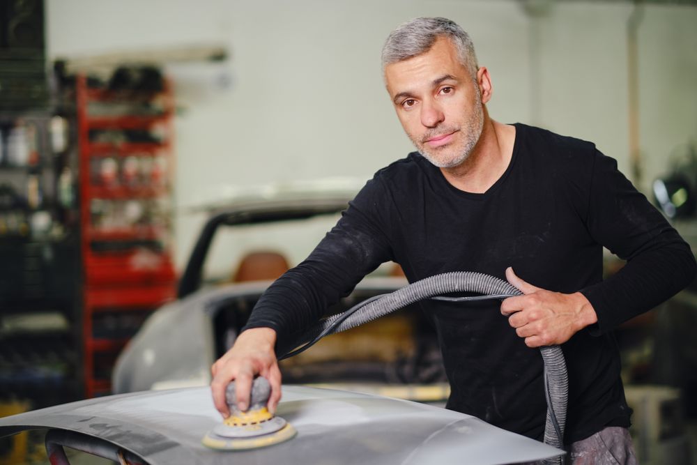 Mechanic grinding paint from car detail
