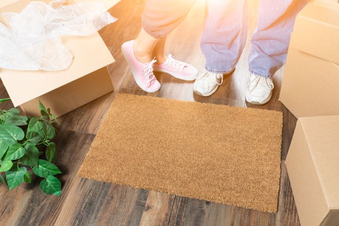 Man and Woman Standing Near Home Sweet Home Welcome Mat, Moving Boxes and Plant