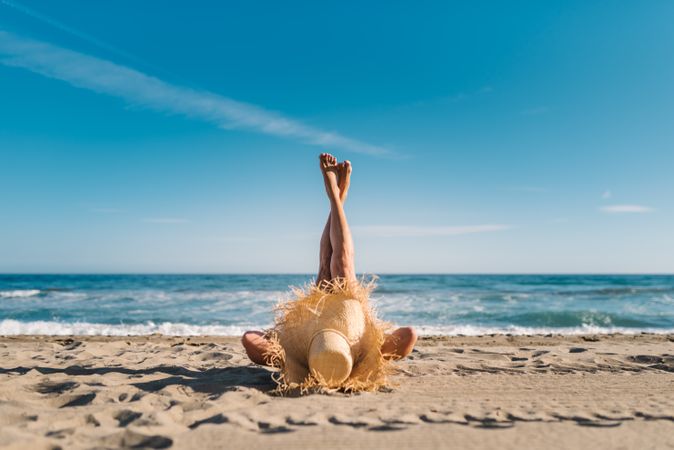 Woman in big hat lying on sandy beach