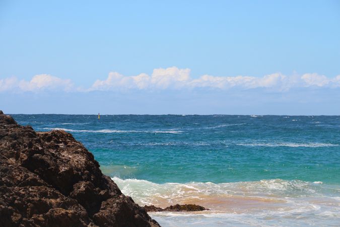 Ocean waves crash against rocks under a clear blue sky at a tranquil beach location on a sunny day