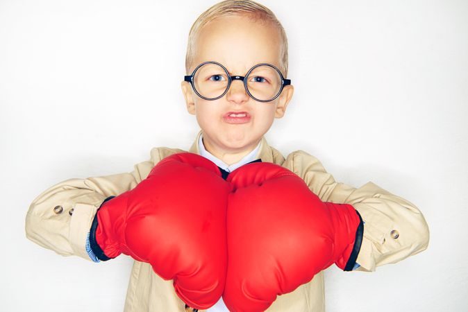 Serious blond boy with a fighter’s face wearing round glasses and punching his red gloves together